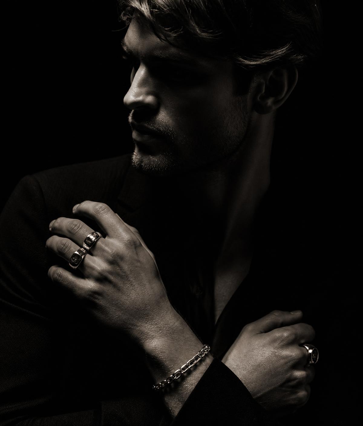 Hands wearing heavy sterling silver rings and a bracelet in dramatic light